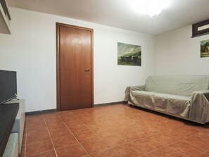 A room with a wooden door, a covered sofa, a tiled floor, and a painting on the wall. - Sondolo by Interhome (Pescia)