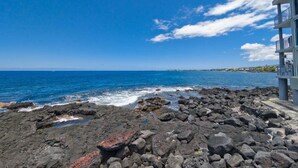 A rocky shoreline with a building on the right. - Little Kona Getaway with AC & heated oceanfront pool 1 BD 1 BA with sleeper sofa (Kailua Kona)