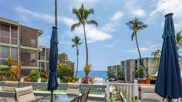 A resort with outdoor seating, palm trees, and a view of the ocean. - Little Kona Getaway with AC & heated oceanfront pool 1 BD 1 BA with sleeper sofa (Kailua Kona)
