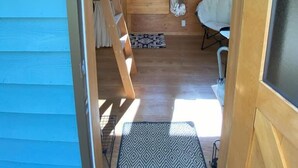 Interior compacto de autocaravana con suelo de madera, una litera, una pequeña cocina y una ventana que proporciona luz natural.