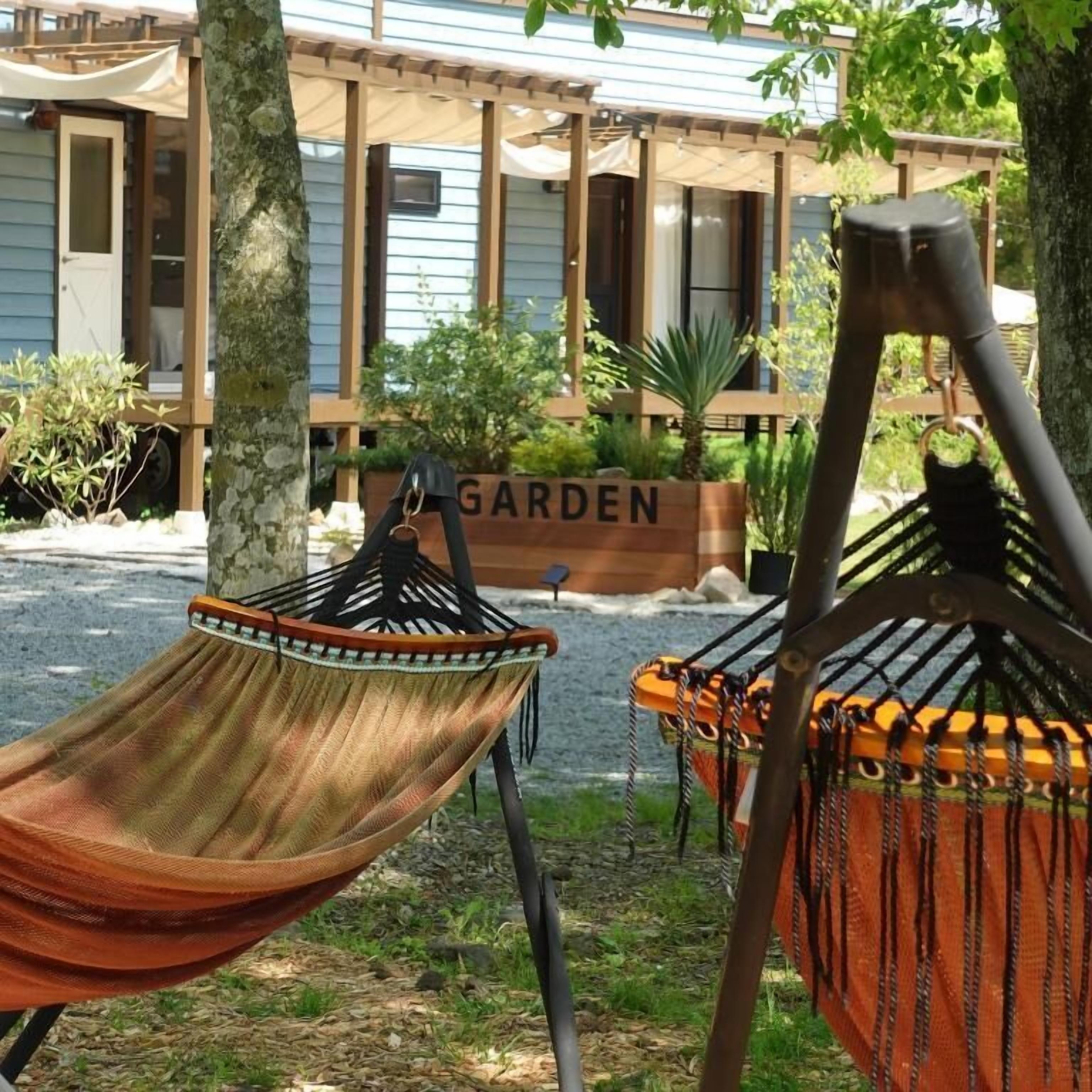 Eine Hängematte, ein Holzdeck und ein Pflanzgefäß mit der Aufschrift 'GARDEN' in einem Garten.