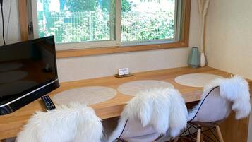 A dining area with a TV, remote, and fluffy chairs.