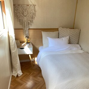 Un dormitorio con una cama, una mesita de noche con lámpara, un colgador de macramé y un cabecero de madera.