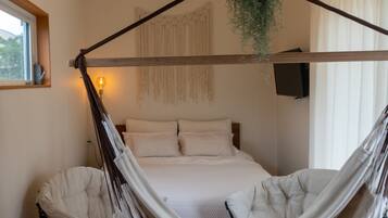 Ein Schlafzimmer mit Bett, einer Hängematte, einem Sessel, einer hängenden Pflanze und einem am Wand montierten Fernseher.