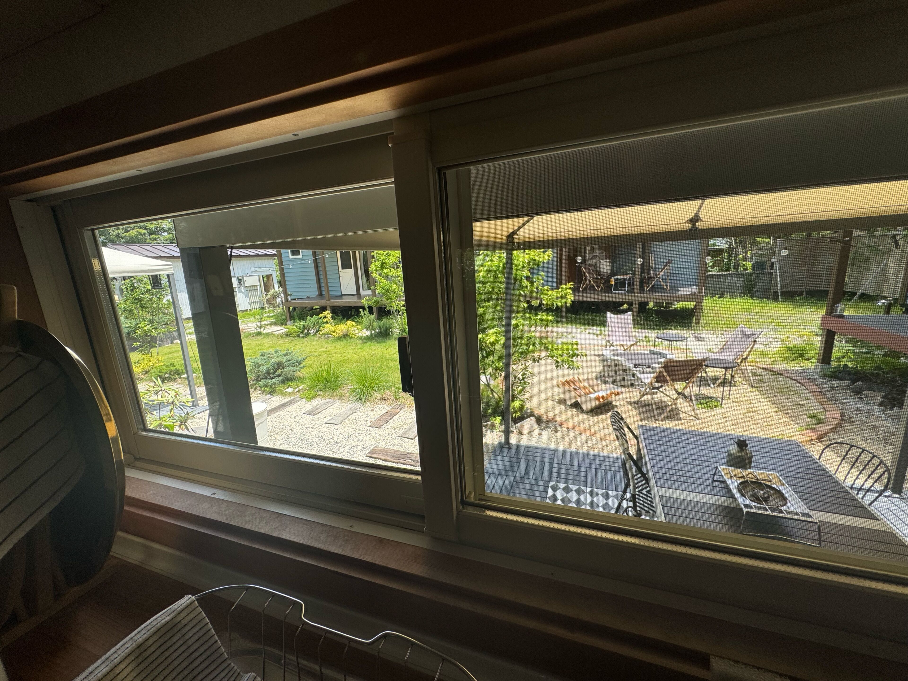 A room with a large window overlooking a backyard with a patio, outdoor furniture, and a grill.