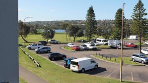 A parking lot with various vehicles, a clear sky, and a body of water in the background. - Beachfront Studio, Views, Best Location (Dee Why)
