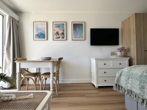 Ein Zimmer mit Esstisch, Stühlen, einem an der Wand befestigten Fernseher und einem Schrank.