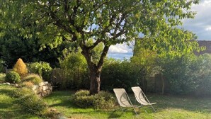 A garden with a large tree, two lawn chairs, and a stone wall. - Les Clés du Boudoir: Charm and Elegance Near Hautefort & Montignac. (Saint Rabier)