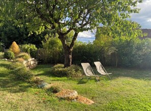 A garden with a large tree, two lawn chairs, and a stone wall. - Les Clés du Boudoir: Charm and Elegance Near Hautefort & Montignac. (Saint Rabier)