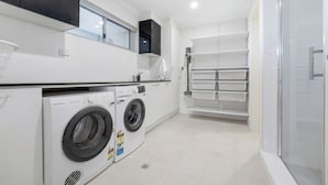 A modern laundry room with a washing machine, dryer, and a glass shower enclosure. - Bayview Luxe Retreat | Luxury Central Coastal Escape with Panoramic Water Views (Tascott)