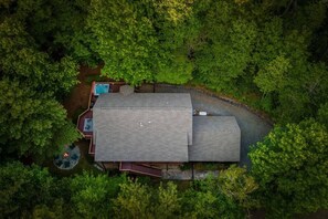 Luftaufnahme eines Hauses, umgeben von dichtem Wald, mit einem Pool und einer Terrassenfläche.