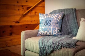Ein gemütliches Zimmer mit einer Holzwand, einem grauen Sofa und einem Kissen mit dem Aufdruck 'WANDER & WONDER'.