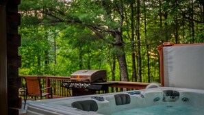 A hot tub and a grill on a wooden deck with a forest backdrop. - Luxury Cabin for Riders Hikers & Anglers +Hot Tub (Pisgah Forest)