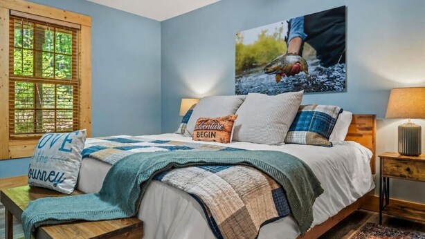 A bedroom with a bed, pillows, a blanket, a window, a painting, and a bedside table. - Luxury Cabin for Riders Hikers & Anglers +Hot Tub (Pisgah Forest)