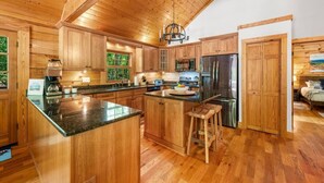 A spacious kitchen with wooden cabinets, a large island, stainless steel appliances, and a chandelier. - Luxury Cabin for Riders Hikers & Anglers +Hot Tub (Pisgah Forest)
