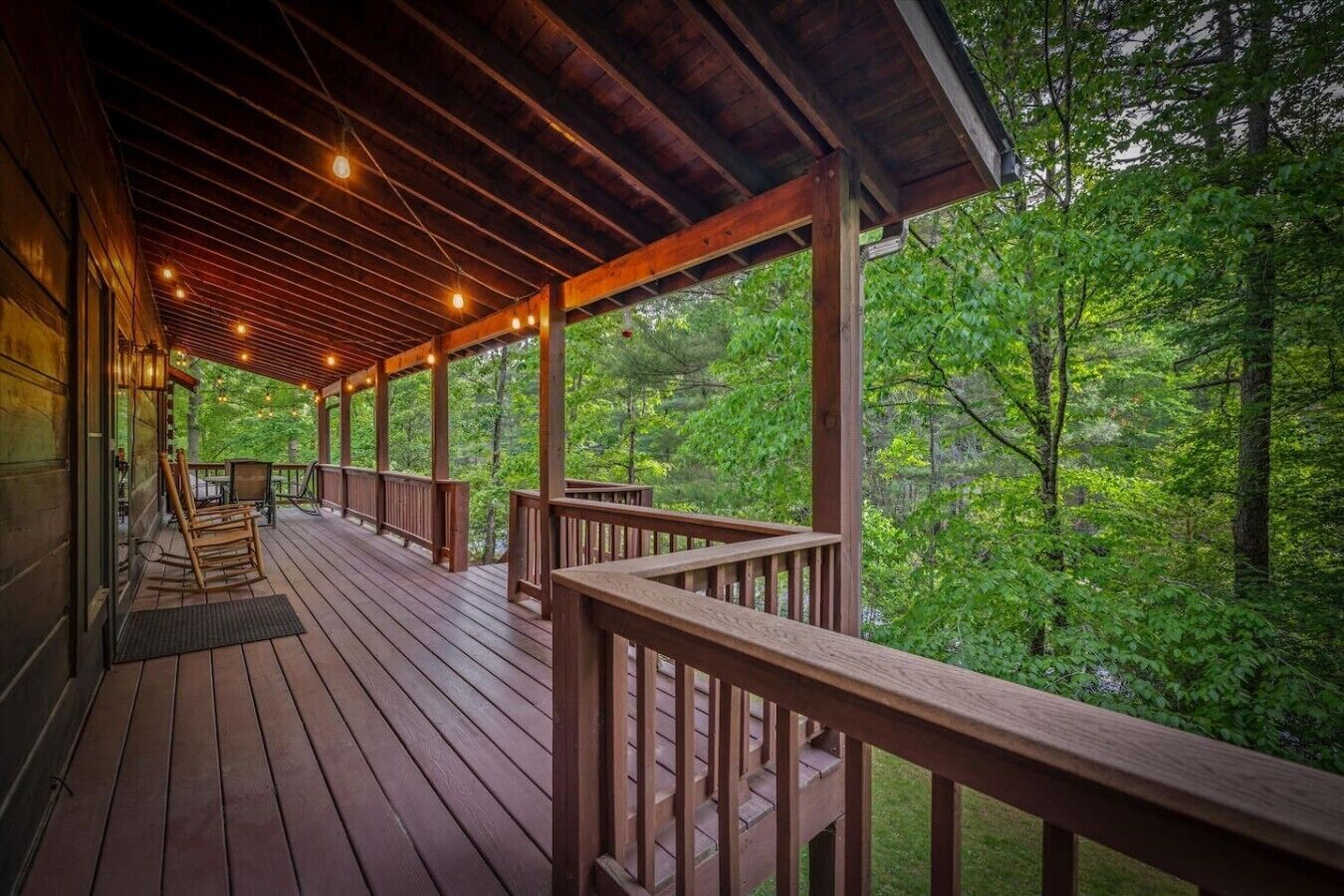A wooden deck with railings, string lights, and a view of a forest.