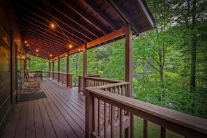 Un terrazzo in legno con ringhiere, luci decorative e vista su una foresta.