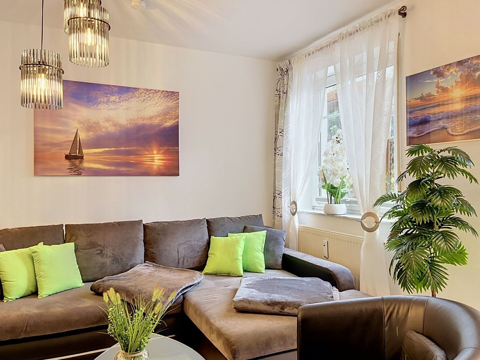 A living room with a sofa, cushions, a plant, and artwork.