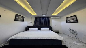 Un dormitorio con cama, mesitas de noche, un ventilador y una obra de arte en la pared.