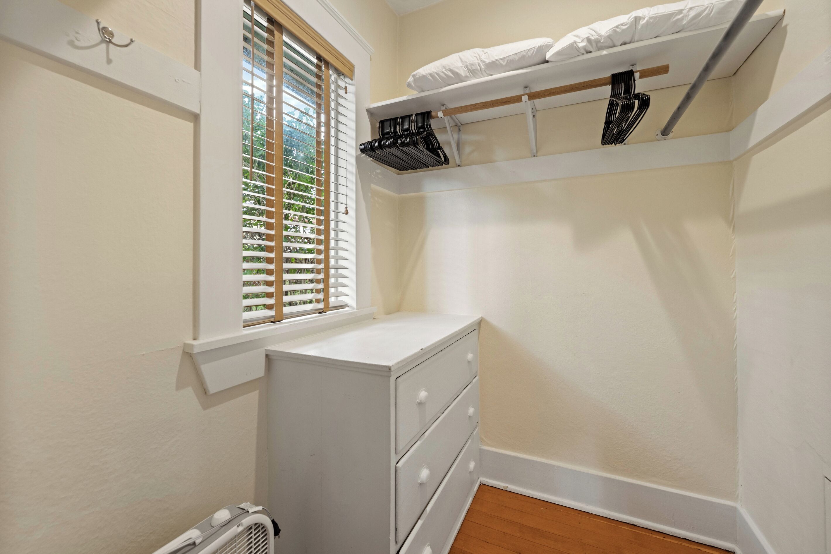 A small, white closet with a window, a radiator, and a shelf above the door.