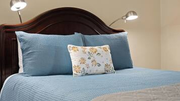 A bed with a blue textured bedspread, a floral pillow, and two bedside lamps.