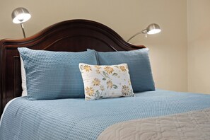 Un llit amb un mantell blau amb textura, un coixí floral i dues làmpades de nit.