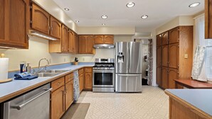 A modern kitchen with wooden cabinets, stainless steel appliances, and a tiled floor. - U-District 1 Bedroom Craftsman w/ Fenced Yard (Butte)