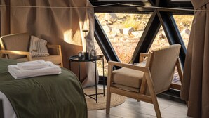 Ein Zimmer mit einem Bett, einem Sessel, einem kleinen Tisch mit Gläsern und Blick durch ein Fenster.