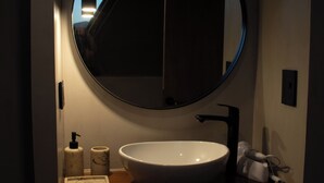 Ein Badezimmer mit rundem Spiegel, Waschbecken in Weiß, Handtuch und Seifenspender.