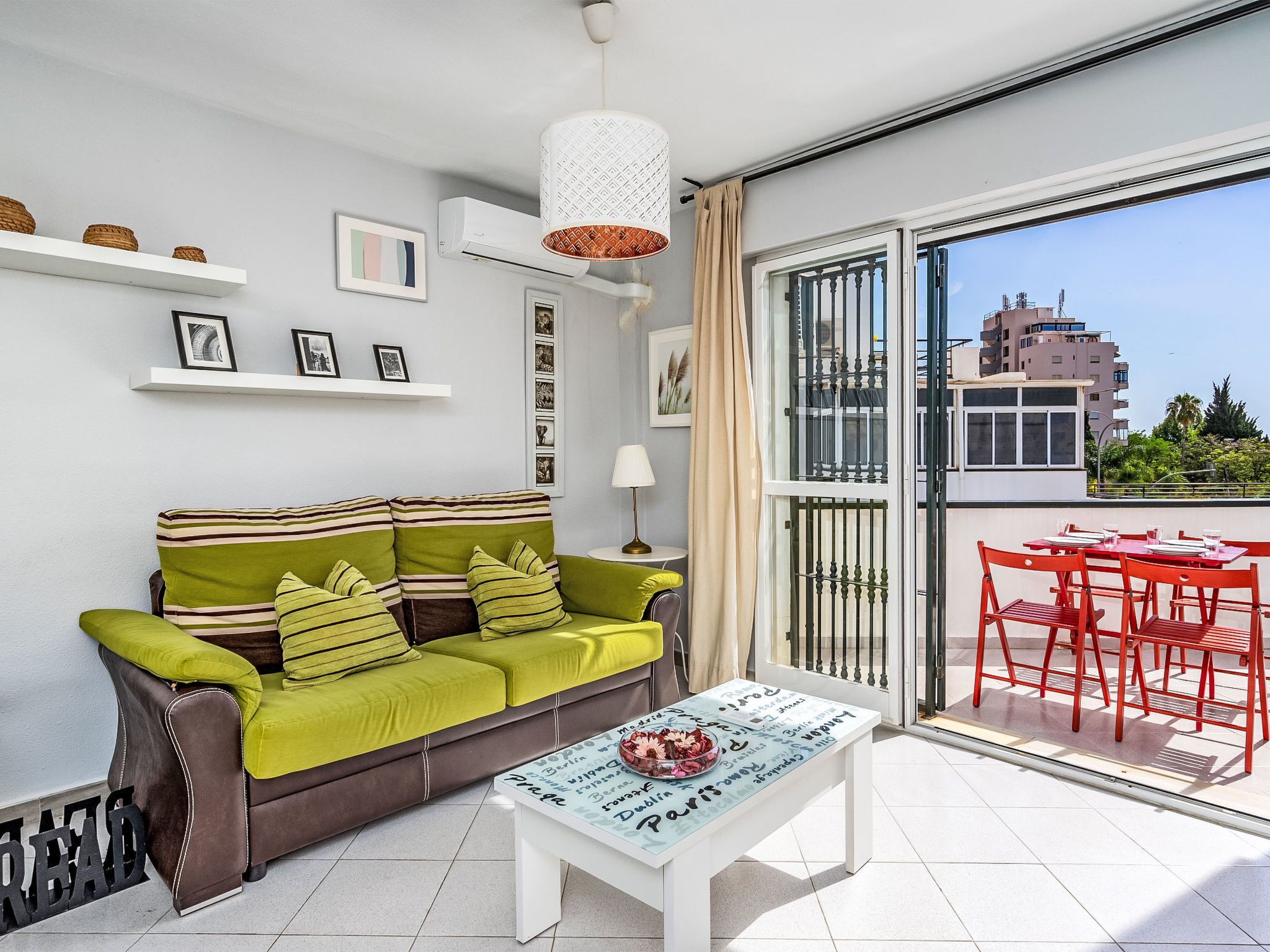 A modern living room with a sofa, a coffee table, and a balcony with red chairs.