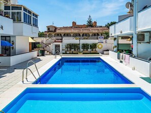 Ein Swimmingpool mit klarem, blauem Wasser, umgeben von weißen Gebäuden, einer Treppe und Topfpflanzen.