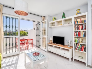 Ein modernes Wohnzimmer mit Fernseher, Bücherregalen, einem Essbereich mit roten Stühlen und einem Balkon mit Aussicht.