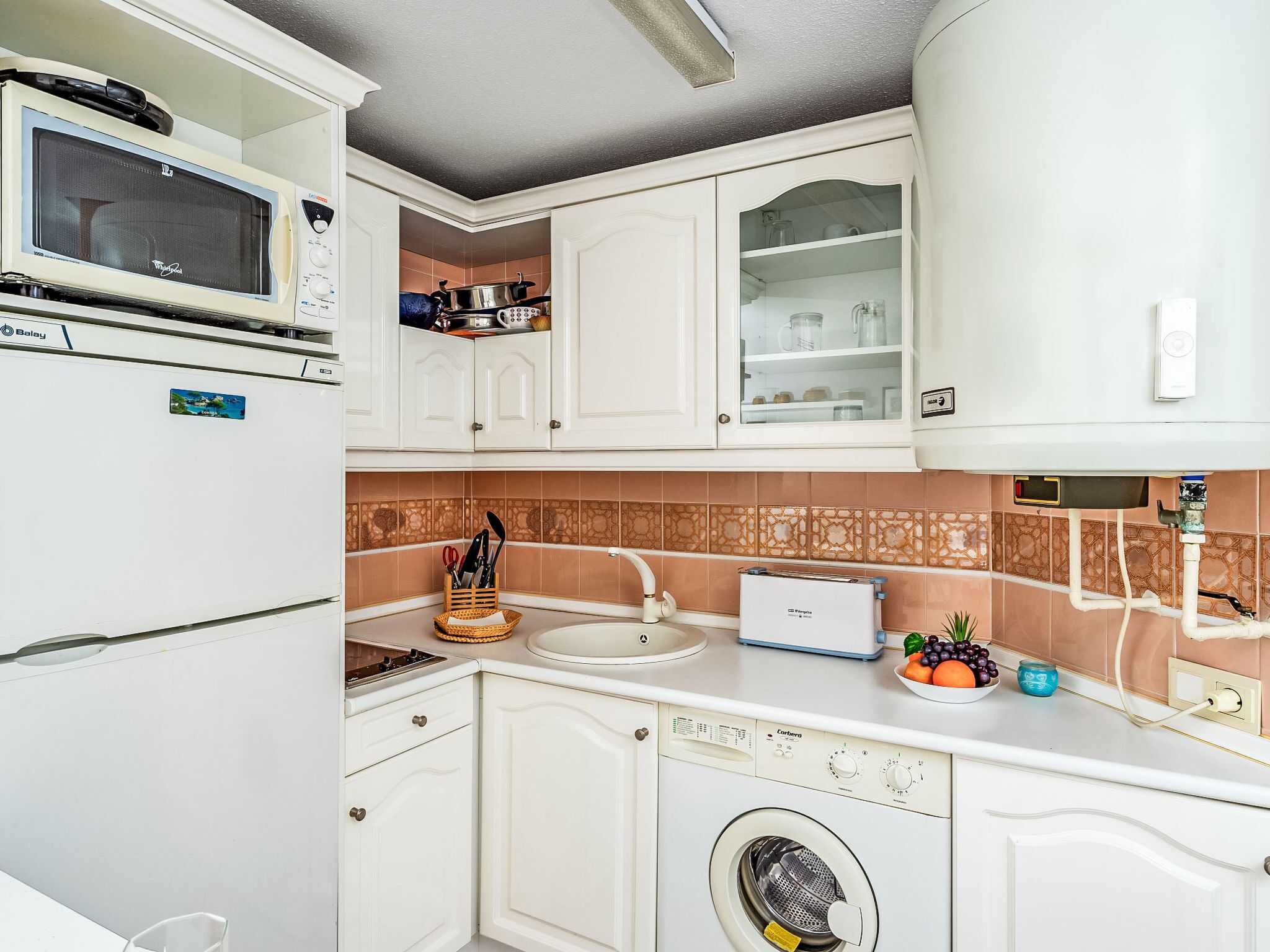 A compact kitchen with a microwave, stove, sink, and washing machine.