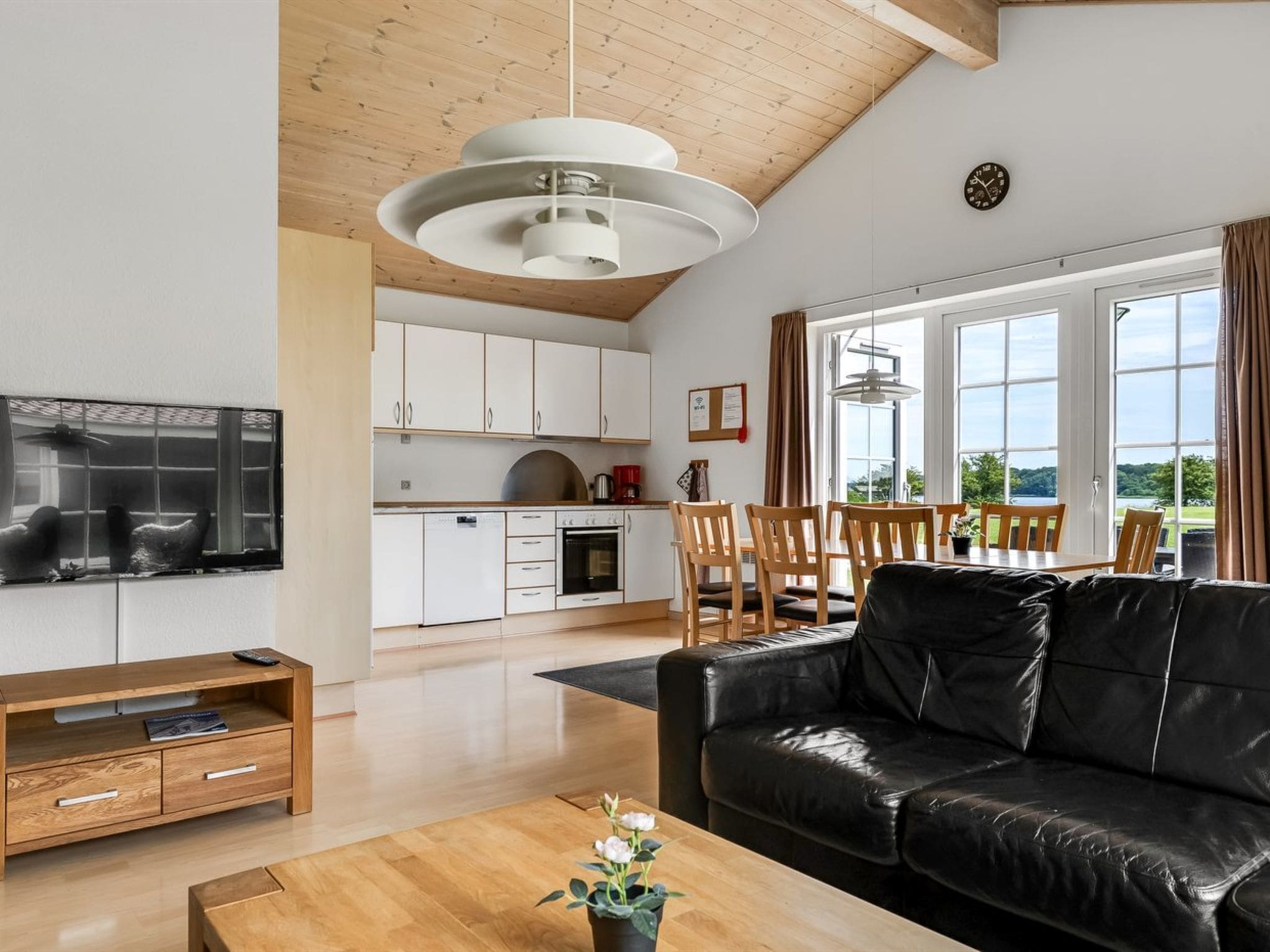 Una sala de estar moderna con un sofá de cuero negro, una mesa de centro de madera y un televisor sobre un mueble de madera.