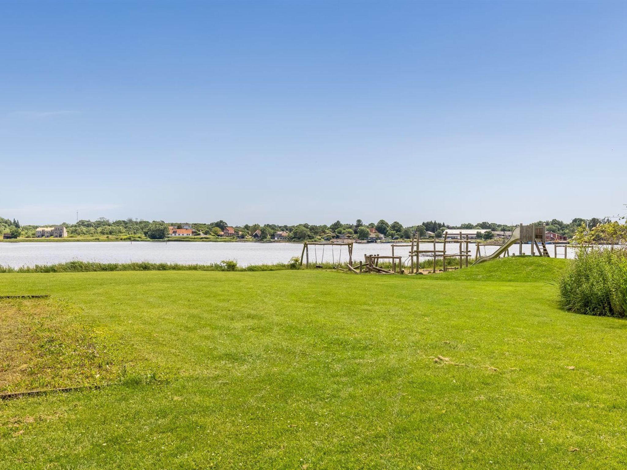 A grassy area with a playground and a body of water in the background.