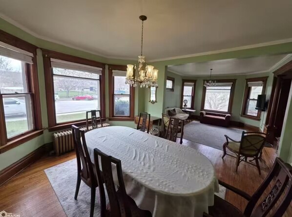 A dining room with a round table, chairs, a chandelier, and large windows. - The Gardens Victorian W/Hot tub and close to town (Clear Lake)