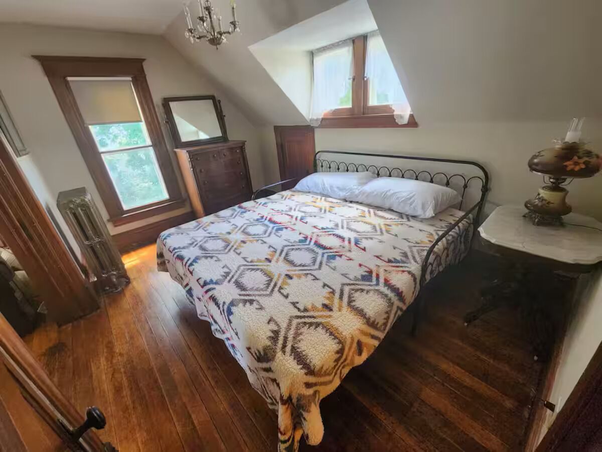 A bedroom with a bed, a dresser, a window, and a chandelier.