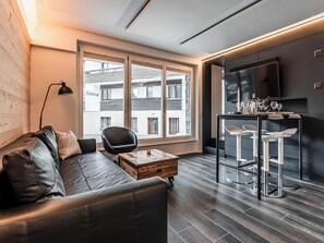 Ein modernes Wohnzimmer mit einem Ledersofa, einem Couchtisch, einem schwarzen Sessel und einer Bar mit Barhocker.