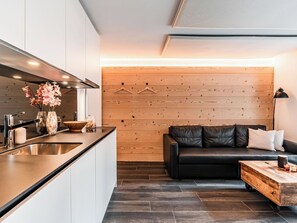 A modern kitchen with a black countertop, stainless steel sink, and a wooden wall with a hanging light fixture. - Kusi's Ranch Studio Studio Nr. 2 Stecknadelhorn by Interhome (Saas-Fee)