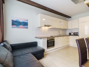 Eine moderne Küche mit weißen Schränken, einem eingebauten Backofen und einem Essbereich mit einer schwarzen Ledersofa und einem Sessel.