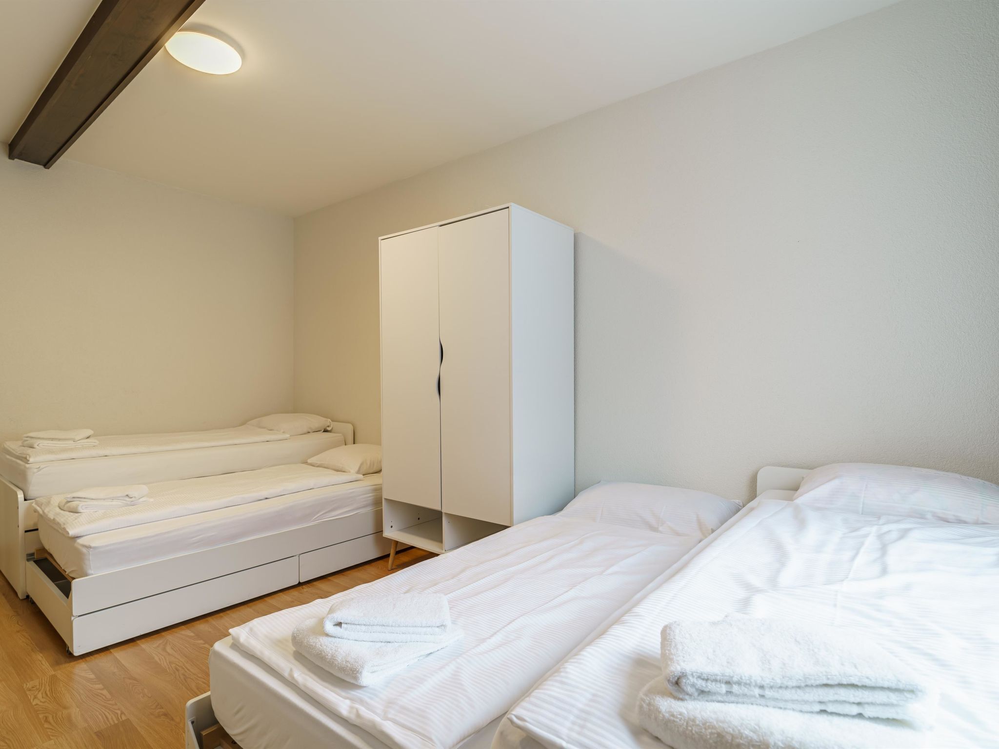 A bedroom with two beds, a wardrobe, and a ceiling light.