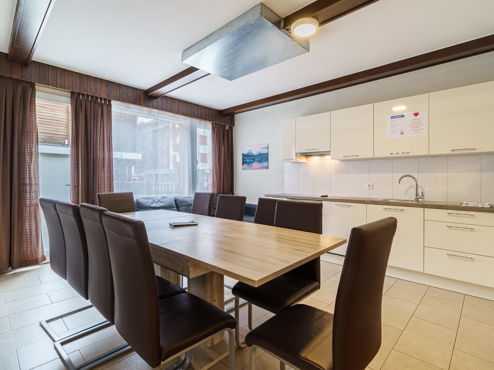 A modern kitchen with white cabinets, a stainless steel sink, and a dining area with a wooden table and leather chairs.