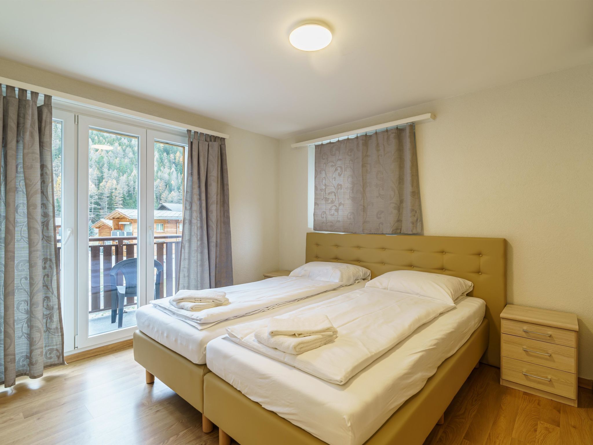 A double bed with a headboard, a bedside table with drawers, and a window with curtains.