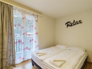 Ein Schlafzimmer mit einem Bett, einem Fenster mit Vorhängen und einer Wand mit dem Schriftzug 'Relax'.