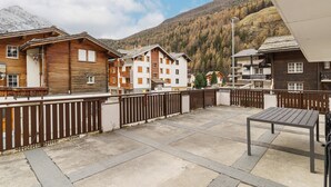 A courtyard with a wooden fence, a table, and buildings with balconies. - Haus Astoria Appartement/Fewo Apt. # 3 by Interhome (Saas-Grund)