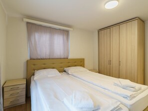 Ein Einzelbett mit Kopfteil, ein Holzschrank, ein Nachttisch und ein Fenster mit Vorhang.