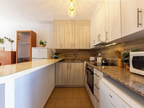 Eine kleine Küche mit Holzausstattung, einer integrierten Mikrowelle und einer Arbeitsplatte aus Granit.