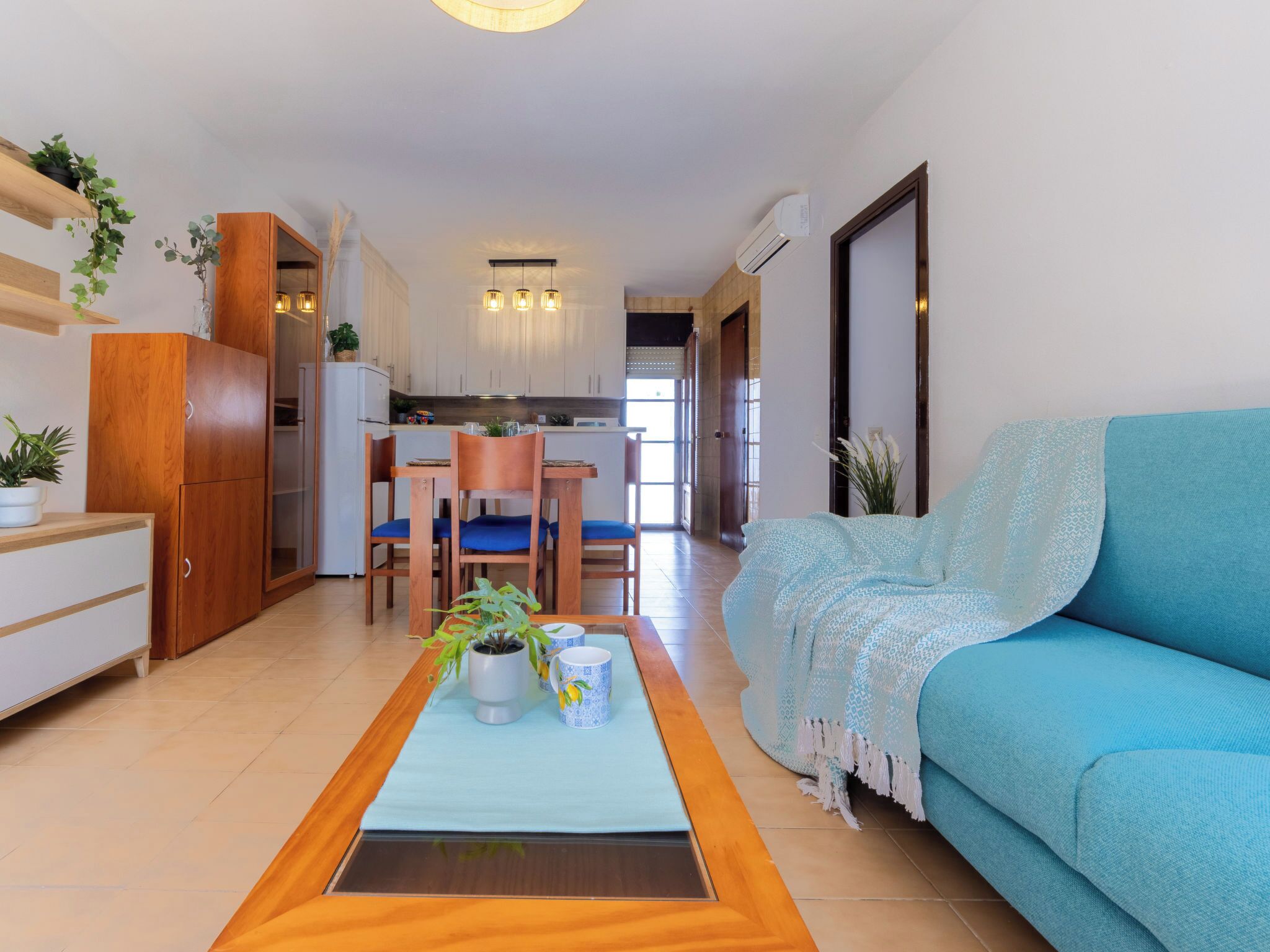 A living room with a sofa, a dining area with chairs, a kitchen in the background, and a view through an open door.