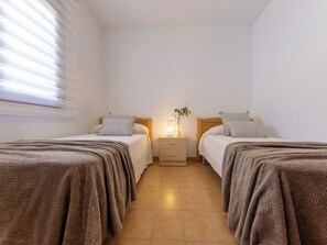 Ein Schlafzimmer mit zwei Betten, einem Nachttisch mit Lampe und einem Fenster mit Jalousien.