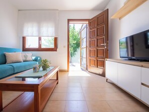Ein Wohnzimmer mit Sofa, Couchtisch, Fernseher und einer zur Terrasse führenden Tür.
